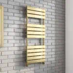 Shiny gold heated towel rail on white brick wall, modern bathroom radiator.